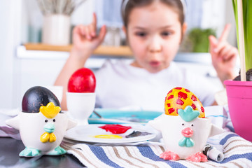 Obraz na płótnie Canvas Little girl paints eggs for Easter in the kitchen at home. Child and holiday items of spring. A happy child draws. Copy space.