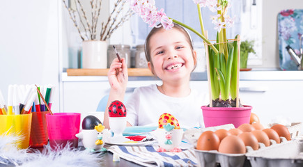 Little girl paints eggs for Easter in the kitchen at home. Child and holiday items of spring. A happy child draws. Copy space.