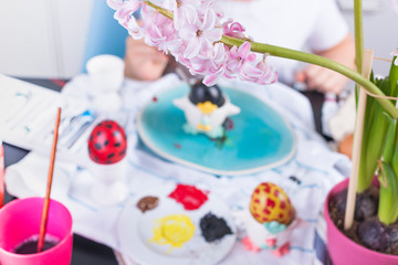 Little girl paints eggs for Easter in the kitchen at home. Child and holiday items of spring. A happy child draws. Copy space.