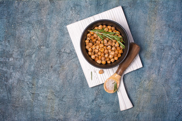 Roasted spicy chickpeas in black bowl with rosemary and sea salt in wooden spoon