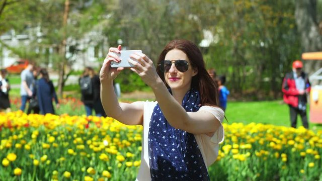 Slow motion woman takes selfies in front of colorful flowers