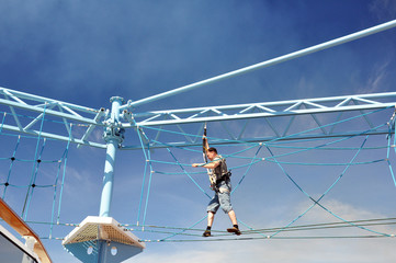a man passes obstacles in a rope Park on the deck of the cruise ship  against the sky and the sea