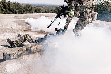 Armed man in camouflage with a sniper gun in his hand, pulling a wounded soldier