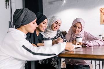 Arab women in hijab, holding and drinking a Cup of coffee, reading a book sitting in a cafe