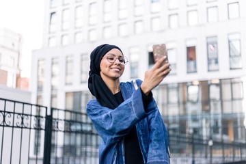 Arab women in everyday hijab traveling through the streets of the city makes a selfie on the phone