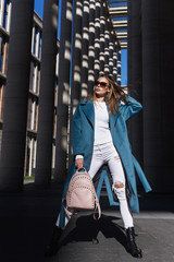 Young beautiful stylish woman walking in blue coat, white jeans and black shoes, holding pink bag...