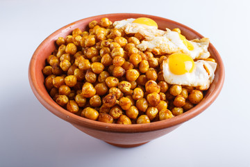 Fried chickpeas with quail eggs and spices in a clay plate isolated on white background.