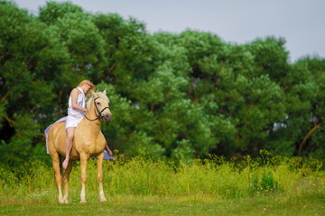 Young rider woman blonde with long hair in a white dress with a train posing and jumping on a...