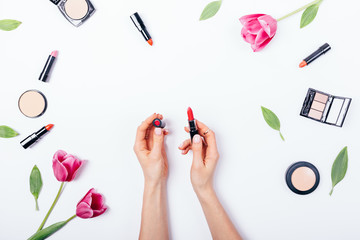 Female's hands holding open classic red lipstick among decorative cosmetics