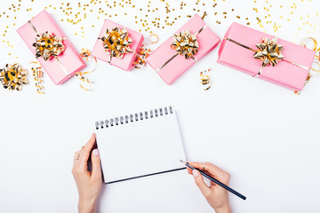 Female's hands writing in blank notepad near festive bright pink gift