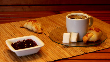 Croissant, cherry marmalade and orange and a cup of coffee on a plate on wooden table
