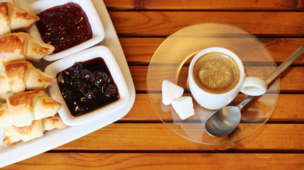 Croissant, cherry marmalade and orange and a cup of coffee on a plate on wooden table