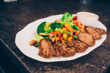 Waiter serving Grilled chicken fillet  meat with vegetable garnish t at restaurant, close up view. Eating and leisure concept. Toned image. Selective focus. Design Gourmet and luxury concept service 