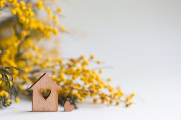 Closeup wooden house with hole in form of heart with yellow mimosa branches on lilac background with copy space. - 256543646