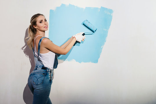 Happy beautiful smiling woman with roller in her hand painting interior wall of new house. New flat renovation concept. White background copyspace
