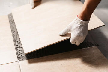 The hands of the tiler are laying the ceramic tile on the floor. Close up macro shot. Home renovation and building new house concept