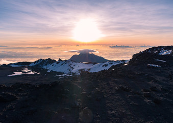 Stunning sunrise view of Mawenzi Peak across the crater at the summit of Kilimanjaro taken from Uhuru Peak. Behind Stella point, Mawenzi sits above the clouds, with a lenticular cloud hanging on top