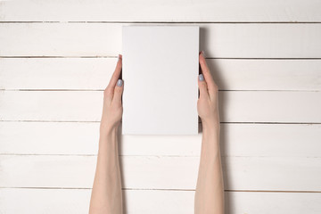 White rectangular box in female hands. Top view. White table on the background