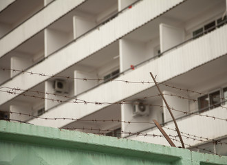 White residential building behind the concrete fence with barbed wire atop. A hotel security at a dangerous country. Focus on a fence