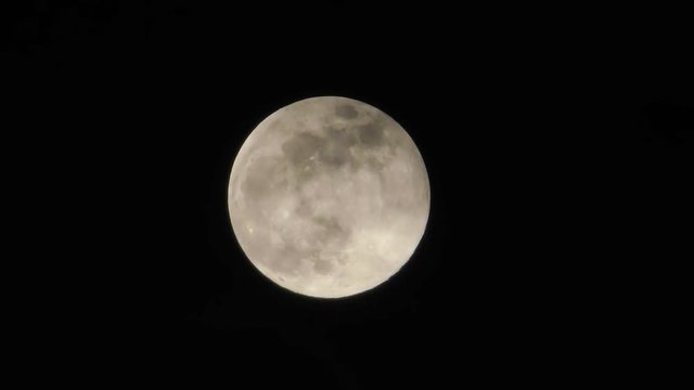 Full moon in night sky. Clouds float along the moon