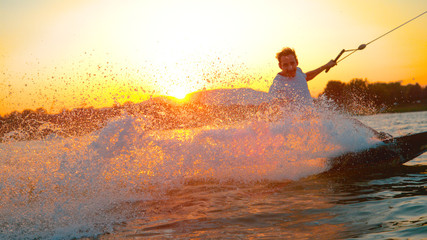 LENS FLARE: Cheerful wakeboarder splashes the lake water at the camera at sunset