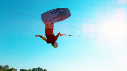 LENS FLARE: Extreme wakeboarder jumping and spinning across the clear blue sky.