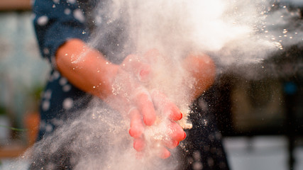 CLOSE UP, DOF: Unrecognizable female baker claps and scatters flour in the air.