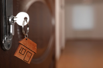 Key with house-shaped trinket in door lock, closeup view