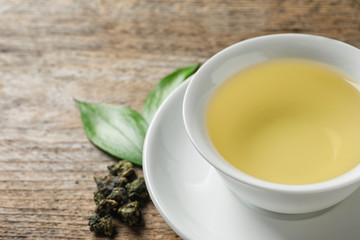 Cup of Tie Guan Yin oolong and tea leaves on wooden table, closeup. Space for text