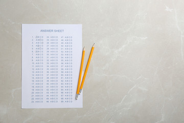 Answer sheet and pencils on grey background, top view with space for text