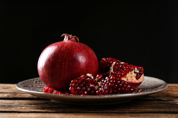 Plate with ripe pomegranates on table against black background