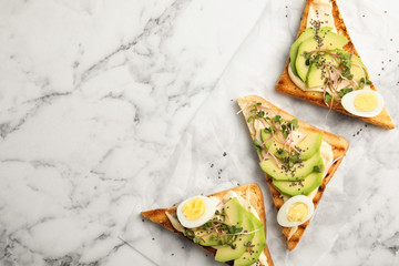 Tasty toasts with avocado, quail eggs and chia seeds on marble background, top view. Space for text