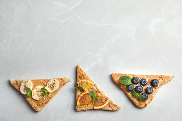 Different toasts with fruits, blueberries, peanut butter and chia seeds on grey background, top view. Space for text