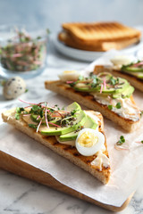 Tasty toasts with avocado, quail egg and chia seeds served on board