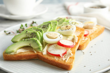 Tasty toasts with avocado, quail eggs and chia seeds on plate, closeup