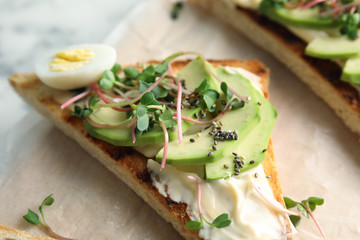 Tasty toast with avocado, sprouts and chia seeds on parchment, closeup