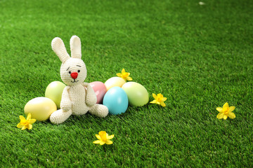 Cute Easter bunny toy and dyed eggs on green grass, space for text