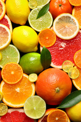 Sliced and whole citrus fruits with leaves as background, top view