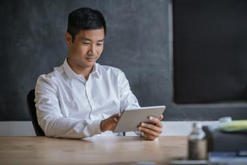 Smiling Asian businessman working on a tablet in an office