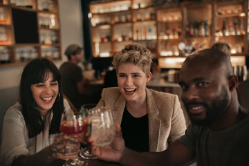 Smiling friends cheering together with drinks at a bar table