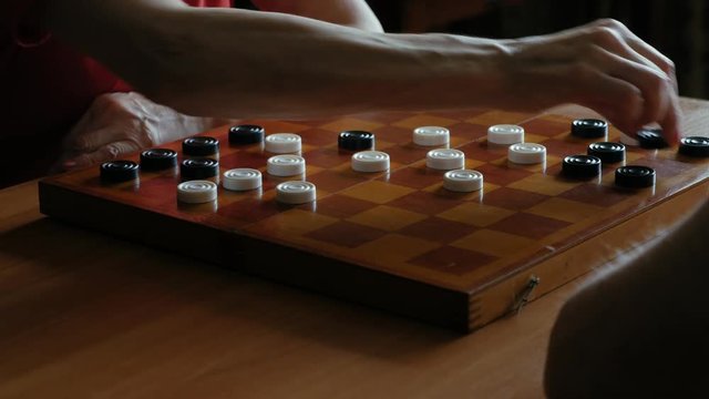 Aged couple playing checkers in Go game on the chessboard at home, close up