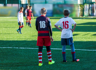 Obraz premium Boys in red white sportswear running on soccer field. Young footballers dribble and kick football ball in game. Training, active lifestyle, sport, children activity concept 