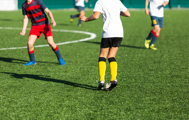 Boys in red white sportswear running on soccer field. Young footballers dribble and kick football ball in game. Training, active lifestyle, sport, children activity concept 