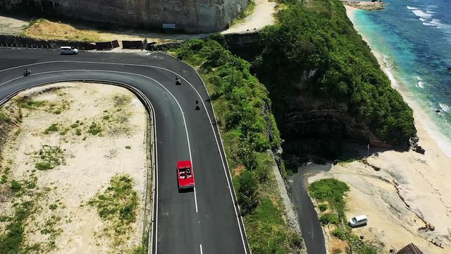 beautiful girl with a gorgeous figure rides on a red cabriolet on a mountain road going down to the sea. 