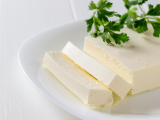 Serbian cheese with parsley on a white plate on a white table. The view from the top. Dairy product.