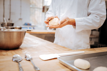 Close up of baker wearing white jacket making little round buns