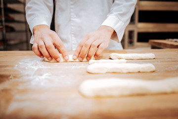 Young baker wearing white jacket forming baguettes on tray