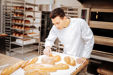 Dark-haired baker touching the loaf of bread after baking the tray