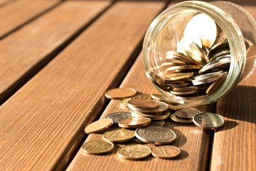Various coins are scattered on a wooden table. The concept of poverty