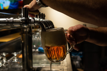Hand of bartender pouring a large lager beer in tap. Rest in a bar with friends